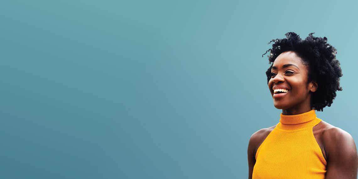 young professional woman in a yellow shirt smiling against a teal background
